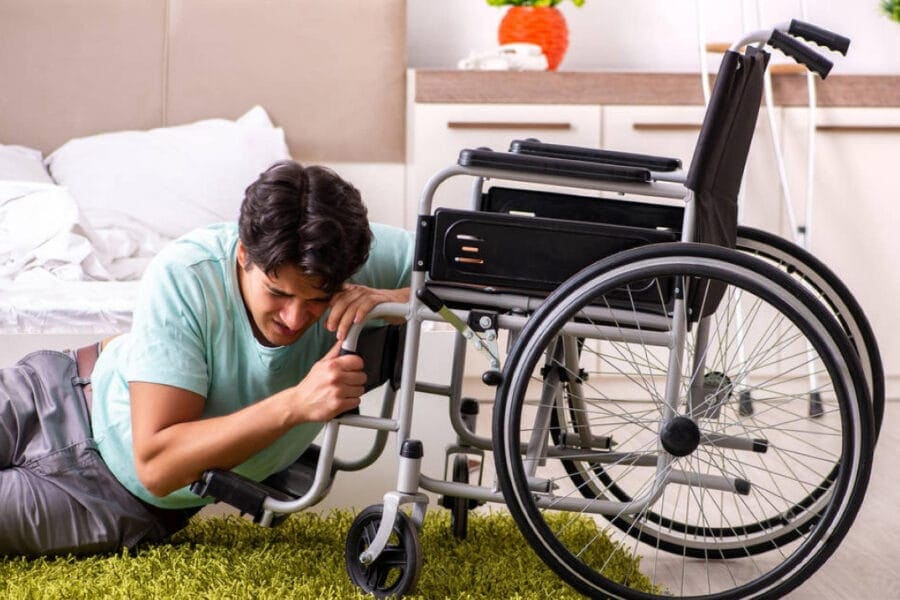 A person is on the floor reaching for a wheelchair next to a bed in a bedroom setting, clearly in need of assistance. A plant and other furniture are visible, subtly reminding one of the importance of common law claim payouts for support and care.