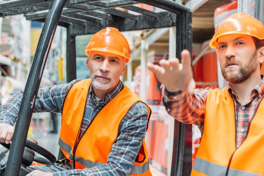workers in hard hat and safety gear drive a forklift in a warehouse