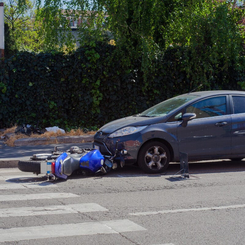 A motorcycle lying on its side in the street next to a damaged car at a pedestrian crossing.