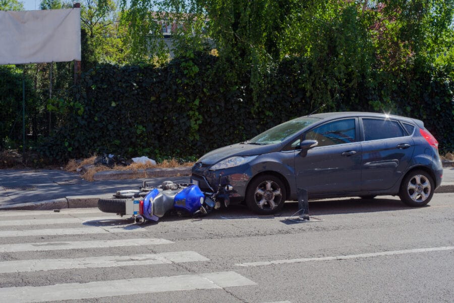 A motorcycle lying on its side in the street next to a damaged car at a pedestrian crossing.