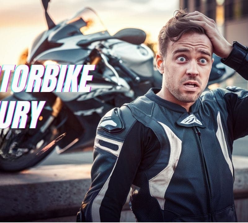 A man in a motorcycle suit looks surprised or worried while holding his head. A motorcycle is parked in the background. The words "Motorbike Injury" are written on the left side of the image.
